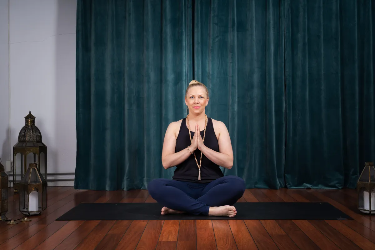 Lina Hammarstrand sitter i skräddarställning med händerna i namaste på yogamattan i studion