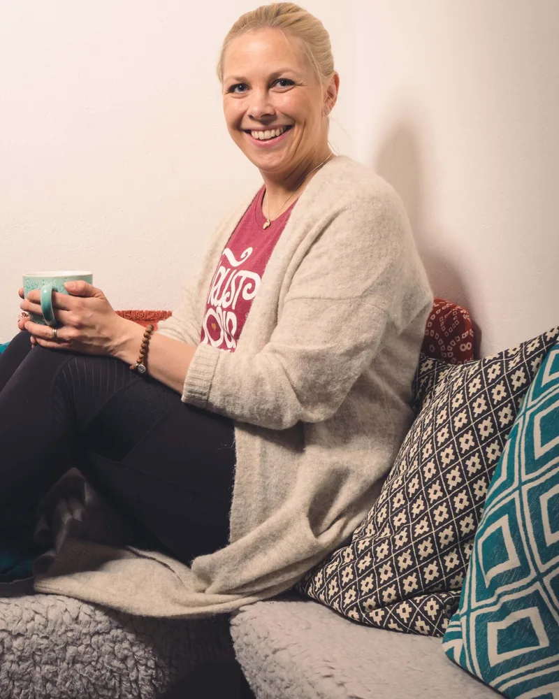 Lina Hammarstrand, diplomerad holistisk coach, med en kopp te i studions soffa
